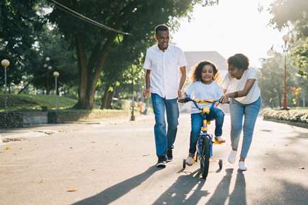 Two adults helping a child learn to ride a bicycle.