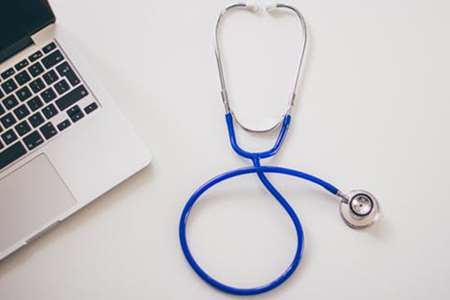 A stethoscope lays on a desk next to a laptop.