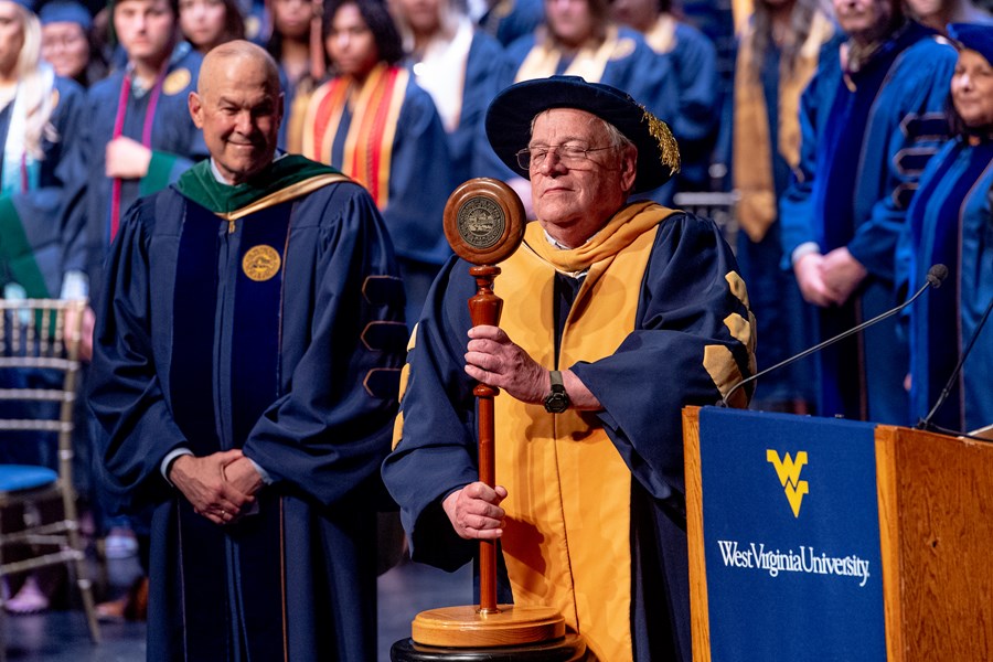 Clinical Associate Professor Michael McCawley stands on the Commencement stage, placing the Mace on its stand.