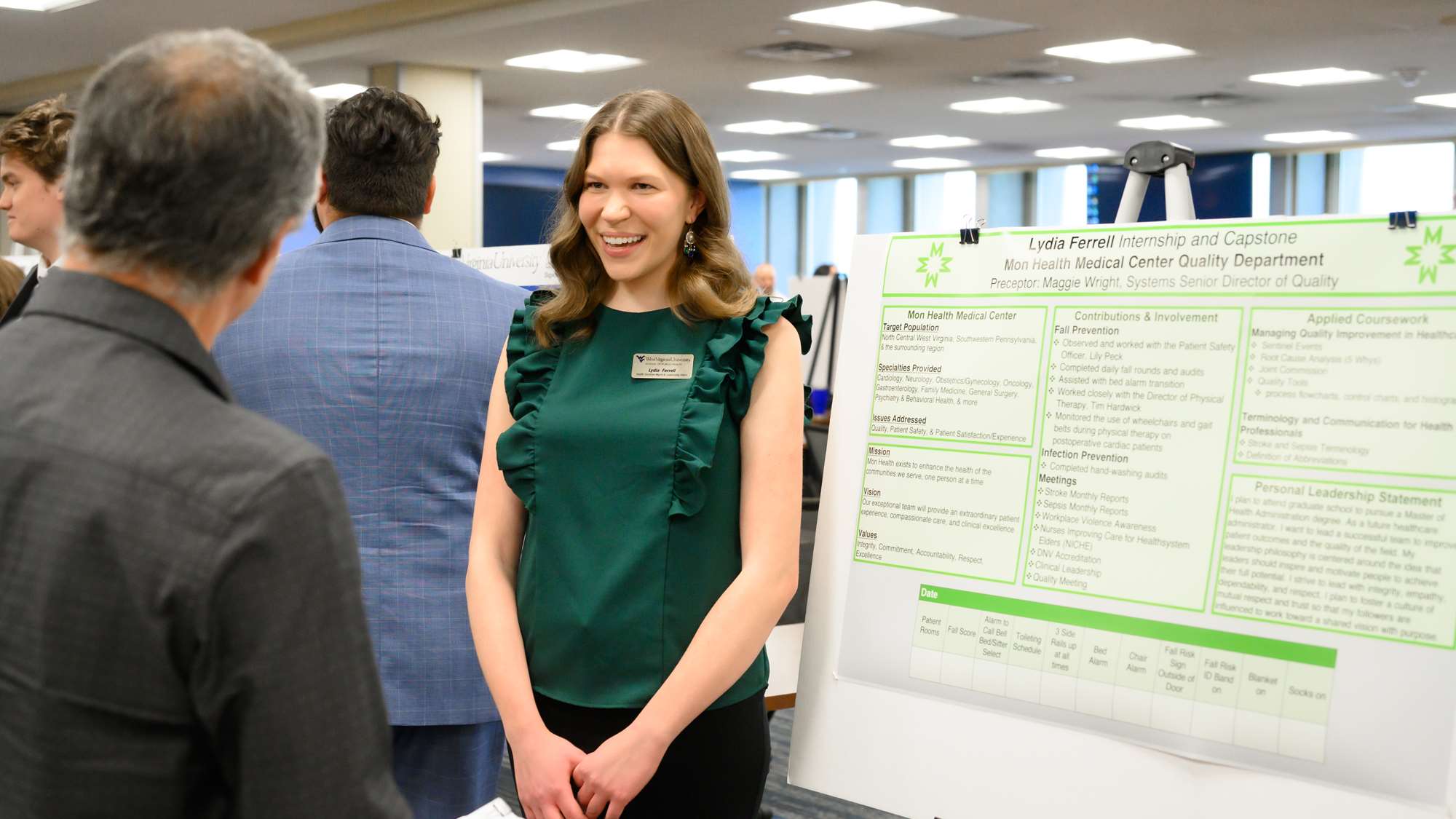 Public Health student Lydia Ferrell stands beside her poster, wearing a green top and smiling as she presents to a faculty member 