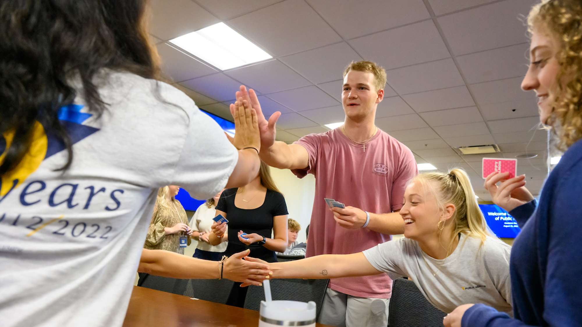 Students stand and touch hands across a table as they engage in a group activity 