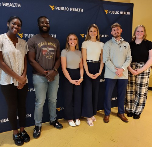 Six students standing in front of WVU School of Public Health backdrop.