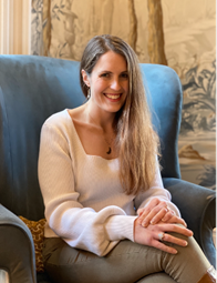 Smiling Elizabeth Claydon seated in blue wing back chair.