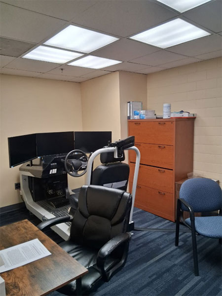 A picture of a room with desks and chairs.  There is a prominent driving simulator as the focus of the room. 