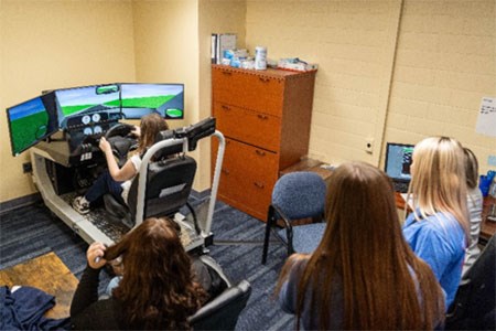Students using the seated simulator while others watch from the rear of the room.