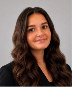 Smiling female with long brown hair. She's wearing a black suit jacket.